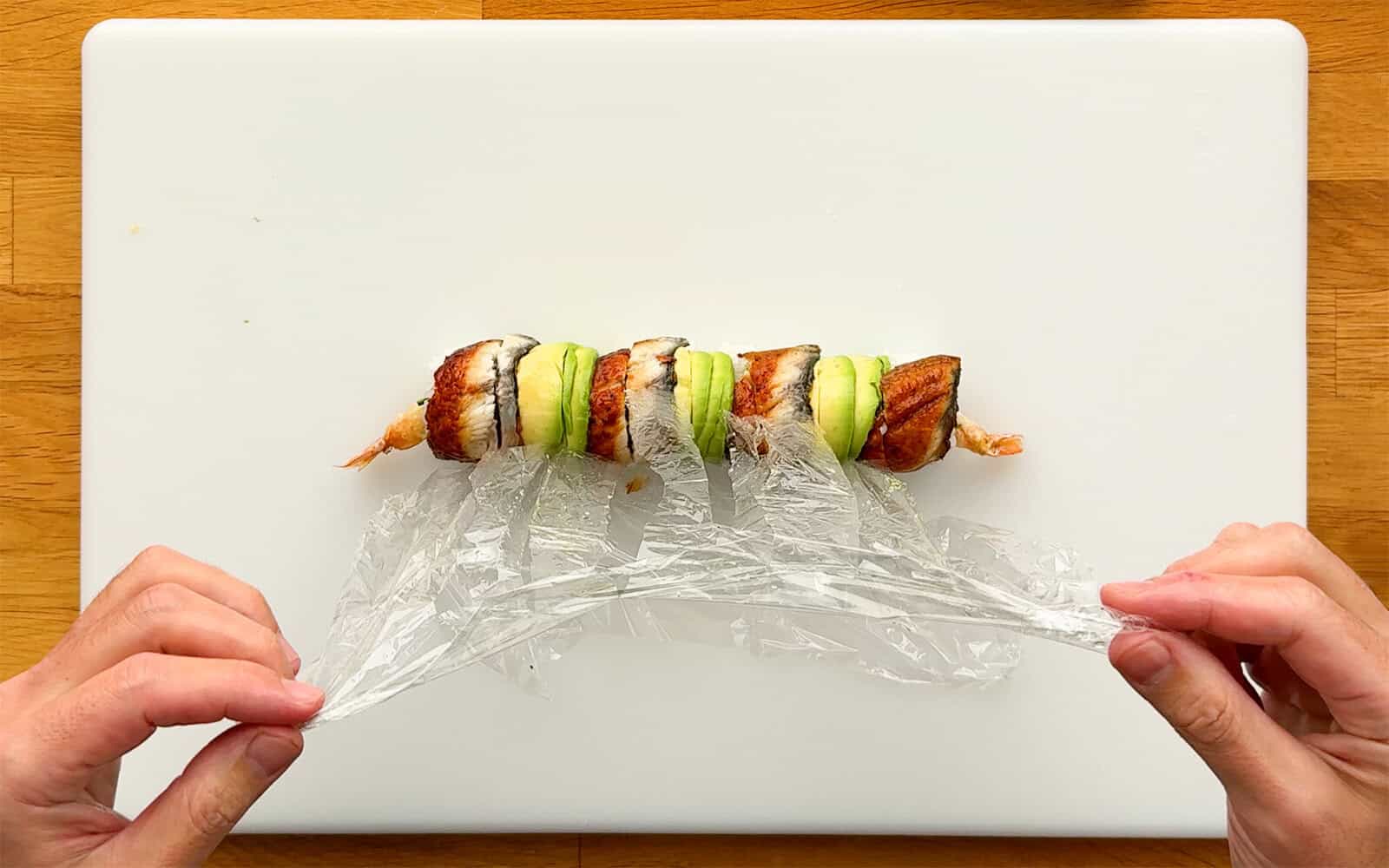 Removing the plastic wrap from a sliced Dragon Roll topped with unagi and avocado.