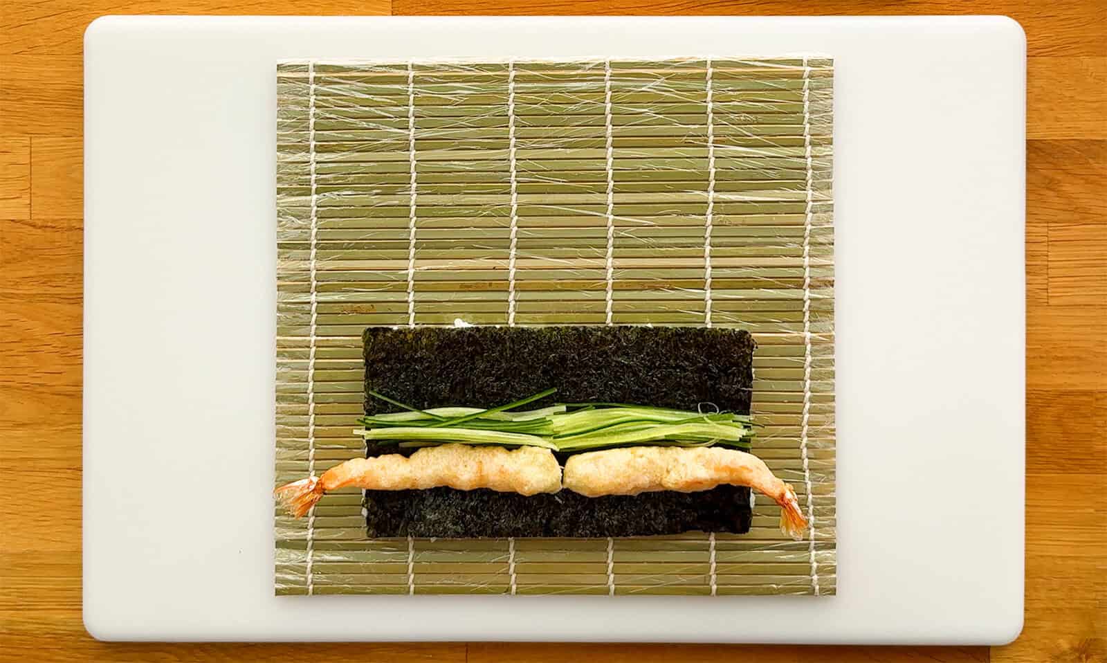 Two shrimp tempura and cucumber strips arranged on nori before rolling a Dragon Roll
