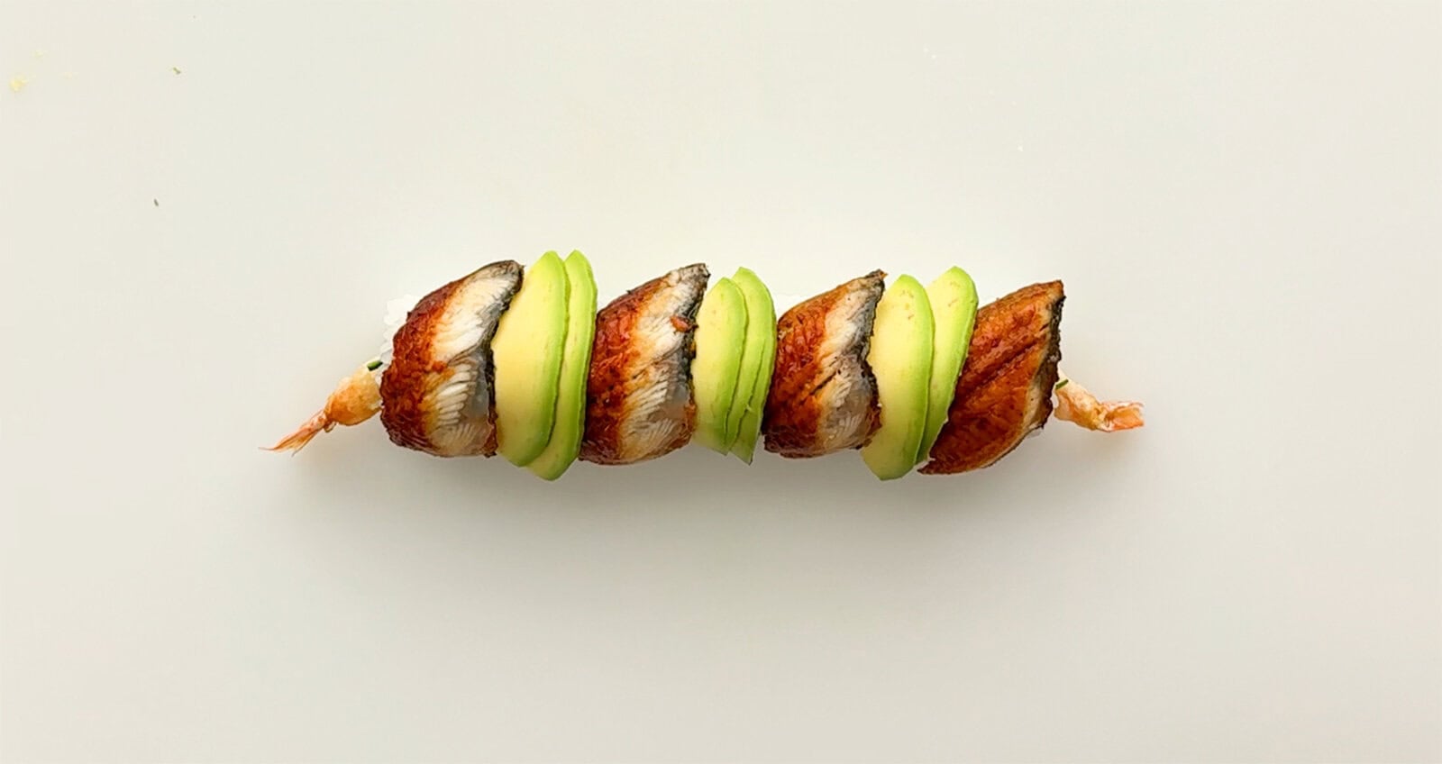 Four slices of broiled unagi alternating with thin avocado slices on top of a homemade Dragon Roll sushi.