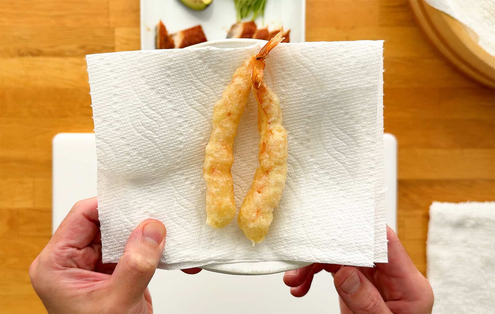 Two freshly fried shrimp tempura resting on a paper towel