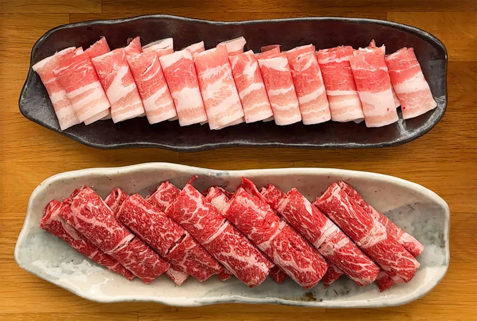 Thinly sliced pork belly and marbled beef arranged on separate plates for Japanese shabu shabu.