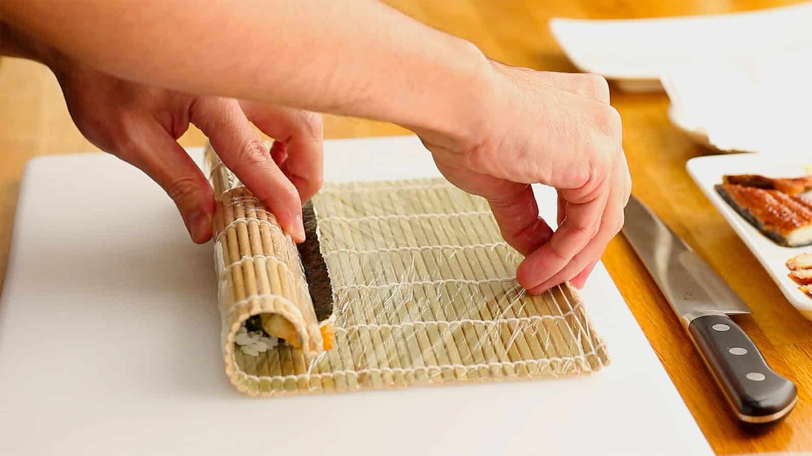 Pulling the bamboo rolling mat away to tighten a Dragon Roll filled with shrimp tempura and cucumber