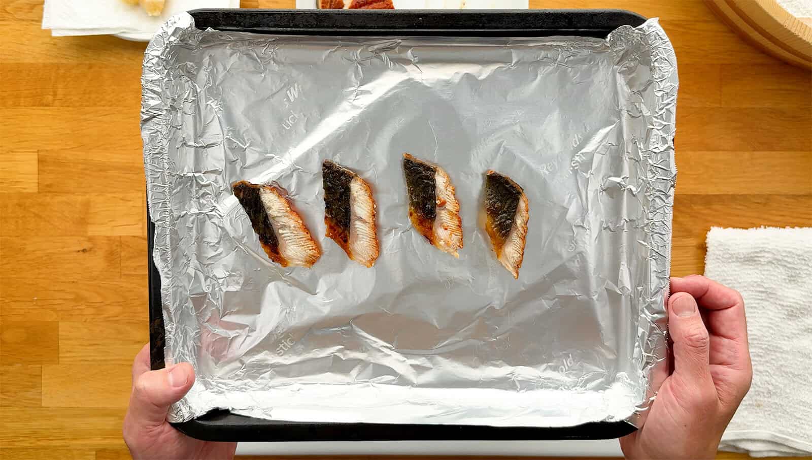 Four slices of unagi placed skin-side up on a foil-lined baking sheet before broiling